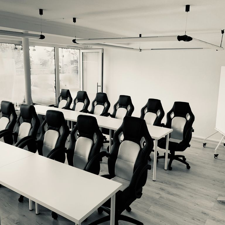 2 Reihen mit je 6 schwarz/weißen Racing-/Gamingstühlen mit weißen Tischen im Fahrschulraum